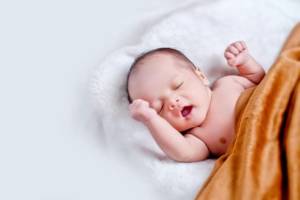 bébé allongé sur fourrure blacnhe avec couverture marron