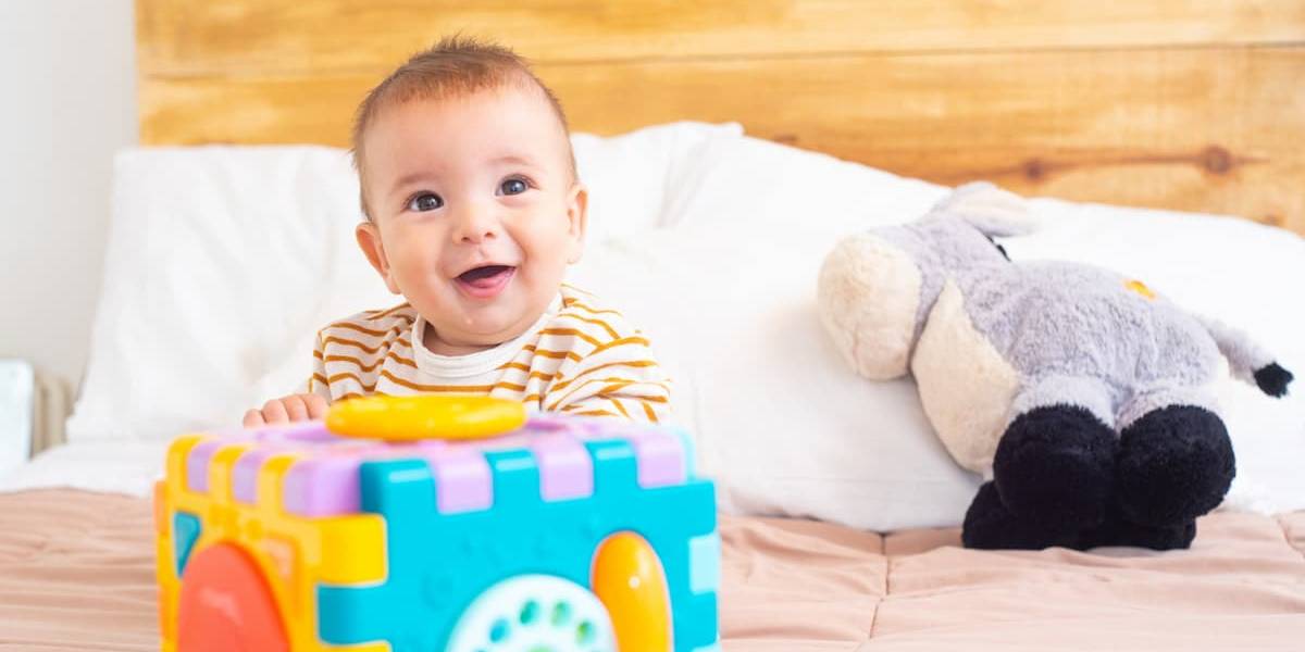 Bébé 10 mois heureux jouant avec ses jouets sur un lit.