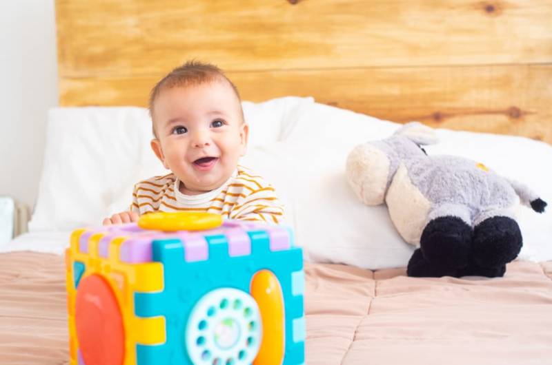 Bébé 10 mois heureux jouant avec ses jouets sur un lit.