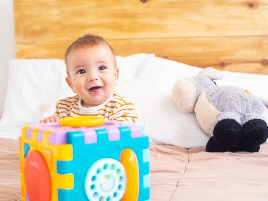 Bébé 10 mois heureux jouant avec ses jouets sur un lit.